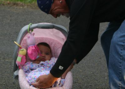 A man leaning down and tucking in a pink blanket around a baby sitting in an infant car seat