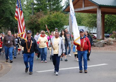 Tribal members leaving Government Hill. Three members are in the front. The member on the right is holding a CTSI flag, the one in the middle is holding the Eagle Staff, and the one on the left is holding the American Flag.