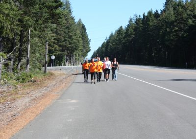 A group of Tribal members walking down the side of the road, one is holding the Eagle Staff